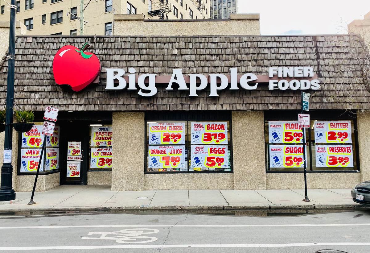 The Big Apple Finer Foods storefront on Clark Street, with a big red apple sign on a shingle roof and hand-painted sale signs in the windows
